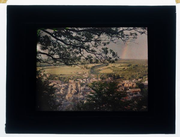 Léon Herlant (1873-1968) — 1 autochrome sur plaque Lumière, 8,5 x 10 cm.  Rare Autochrome d'un Arc-en-Ciel avec Vue sur la Ville de Spa, circa 1910  Cette rareté photographique est un autochrome exceptionnel, capturant un arc-en-ciel en plein éclat, avec la ville de Spa en arrière-plan, vue en plongée. Un instant naturel empreint de magie et de beauté fugace, sa richesse colorée est amplifiée par