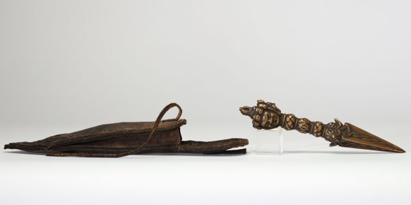 Rare phurba tibétain avec son fourreau, triple lame triangulaire et décoré à la poignée d’une tête de divinité courroucée finement ciselée son fourreau d’origine en cuir gravé, de forme effilée, avec son cordon de suspension, élément rare pour ce type d’objet. probablement XVIIIe siècle