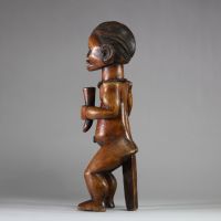 Figure d’ancêtre Fang Mabea ( Byeri), Sud-Cameroun (zones de Kribi, Akom II, Bipindi) . La posture est semi assise, les deux mains jointes tenant une corne de libation, symbole d’offrande aux ancêtres. La coiffure est finement striée, typique du style Fang-Mabea. Un appui dorsal vertical permet de stabiliser la posture. Une scarification frontale est visible entre les sourcils, les prunelles sont