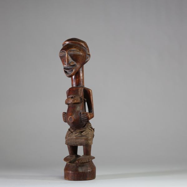 Fétiche rituel figurant un nkishi protecteur ethnie Songye, sous groupe Kalebwe. Figure dotée d'un long cou, de pieds larges, d'un visage souriant et d'une ceinture abdominale contenant une charge organique et présentant autrefois une corne magique au sommet du crâne. Usure rituelle et patine ancienne authentifient son usage. Très belle représentation Kalebwe, entre force symbolique et expressivit