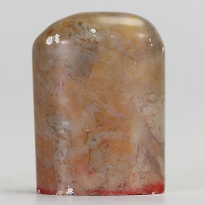 Sceau chinois ancien en pierre dure veinée, gravé à la base de caractères stylisés en rouge  Sceau chinois en pierre naturelle, de forme légèrement bombée, à pâte veinée de tons bruns et orangés. La b