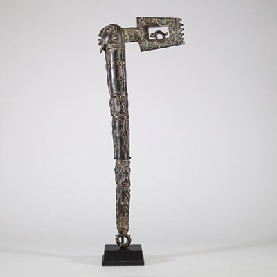 Hache cérémonielle en bronze à riche décor animalier – Afrique, probablement Congo, XXe siècle Hache cérémonielle coulée en bronze à patine foncée, ornée d’un décor finement ciselé figurant une tête anthropomorphe au sommet du manche, et une lame en forme de tranchant rectangulaire ajouré, décoré de motifs concentriques. Le fût présente une remarquable composition en relief représentant une faune