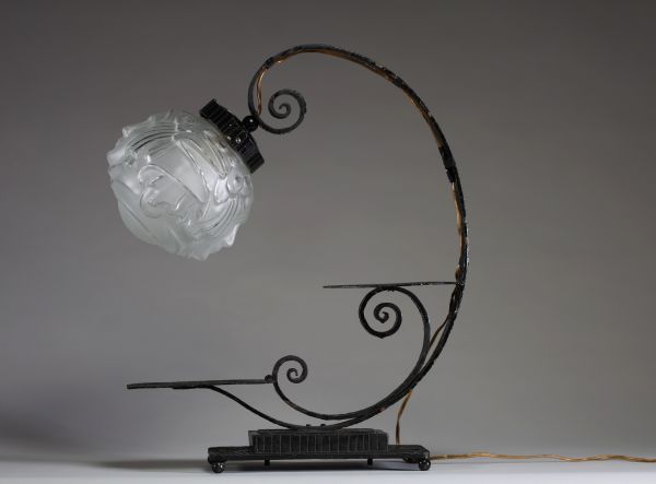 André HUNEBELLE (1896-1985) dans le goût de - Lampe pied fumer en fer forgé martelé et globe en verre moulé pressé à décor de visages de femmes, vers 1920-30.