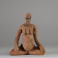 Rare statuette en terre cuite Djenné, Mali. XIème- XIVème siècle apr. J.-C. ( restauré). La figure est représentée assise, les jambes écartées et repliées symétriquement, dans une posture évoquant l’introspection ou le recueillement rituel. Le torse est orné de scarifications en damier et les seins sont traités en relief. Le visage, à la bouche proéminente, conserve des traces de pigments rouges e