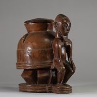 Oracle à souris ( bo num) Baoulé,  côte d’Ivoire. Bois dense, relativement ancien, à patine brune, représentant une figure masculine  assise, soutenant un récipient divinatoire circulaire finement décoré. Un trou circulaire obturé sous la base atteste de l’usage rituel de cette pièce, destinée aux pratiques divinatoires du devin (komien). Le style correspond à la statuaire Baoulé classique du cent