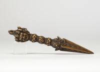 Rare phurba tibétain avec son fourreau, triple lame triangulaire et décoré à la poignée d’une tête de divinité courroucée finement ciselée son fourreau d’origine en cuir gravé, de forme effilée, avec son cordon de suspension, élément rare pour ce type d’objet. probablement XVIIIe siècle