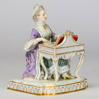Figurine en porcelaine polychrome de la manufacture de Meissen « Jeune femme devant un petit piano ou clavecin. La base à décor moulé de lambrequins dorés repose sur un socle rectangulaire. Marque aux