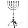 Grande menorah à sept branches en fer forgé, travail juif, vers 1900  Élégante et imposante menorah à sept branches en fer forgé, réalisée par un artisanat juif du début du XXe siècle. La structure finement travaillée, à décor de feuilles stylisées et de volutes, repose sur un piétement tripode à motif végétal. Ce chandelier, emblématique de la tradition rituelle juive