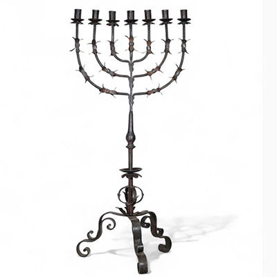 Grande menorah à sept branches en fer forgé, travail juif, vers 1900  Élégante et imposante menorah à sept branches en fer forgé, réalisée par un artisanat juif du début du XXe siècle. La structure finement travaillée, à décor de feuilles stylisées et de volutes, repose sur un piétement tripode à motif végétal. Ce chandelier, emblématique de la tradition rituelle juive