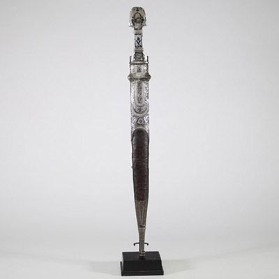 Poignard persan à décor d'argent, début XIXᵉ siècle Poignard oriental monté en argent repoussé et ciselé, présentant une garde et un fourreau richement ornés de motifs floraux et de cartouches géométriques, caractéristiques de l’art décoratif perse. Le pommeau bombé et la garde sont rehaussés de filets floraux, certains émaillés de bleu.  La lame à double tranchant, probablement forgée en acier, e