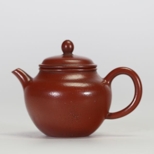 Théière globulaire en terre cuite pourpre, dite zisha, typique de la production de Yixing. Elle présente un panse arrondi, un court bec conique et une anse semi-circulaire.
