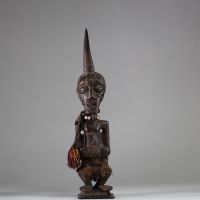 Fétiche Songye Nkisi, sous style Kalebwe, RD Congo. H : 46 cm. Figure masculine en bois, surmonté d’une corne rituelle, visage orné de clous de tapissier à fonction magique. Patine ancienne noire /brune, accessoires rituels suspendus (perles, fibres, cordelettes), cavités sous les bras. Nkisi de protection ou de justice activé par un « Nganga ». Style expressif et puissant propre aux Songye Kalebw