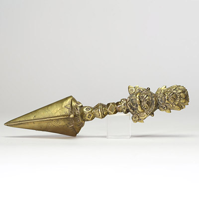 Poignard rituel bouddhique, dit phurba, en bronze doré, à triple lame triangulaire. Le manche est orné d’un nœud symbolique à facettes et se termine par une représentation expressive de Vajrakilaya. Travail tibétain, XIXe siècle.